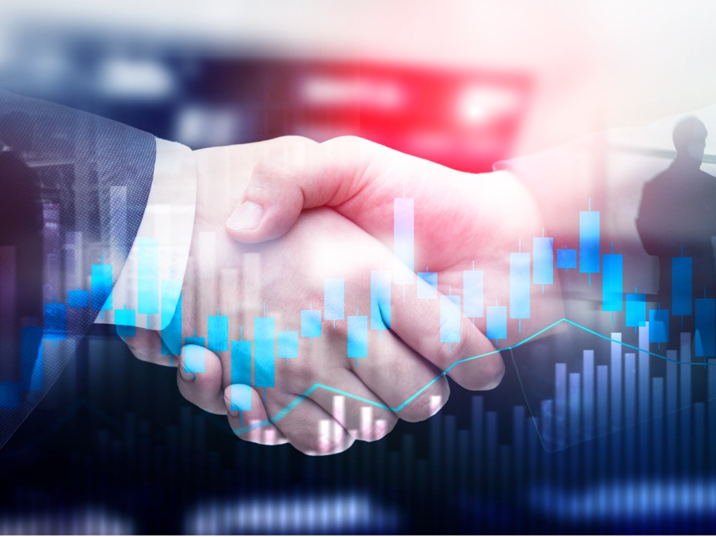 Two business professionals shaking hands with financial graphs in the background, symbolizing a partnership buyout agreement