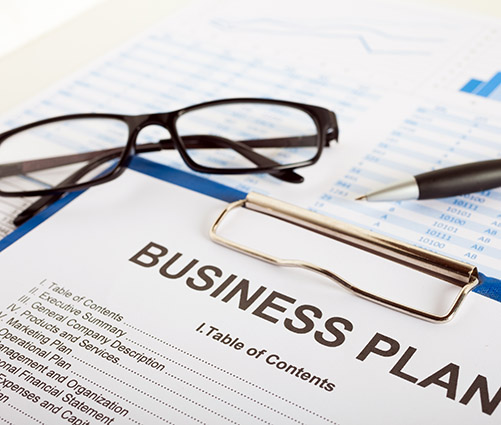 Detailed business plan document with charts, pen, glasses, and clipboard indicating preparation for investor visa citizenship by investment program.